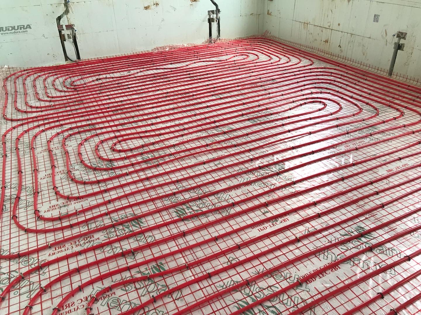 Red underfloor heating pipe loops clipped to mesh over floor insulation