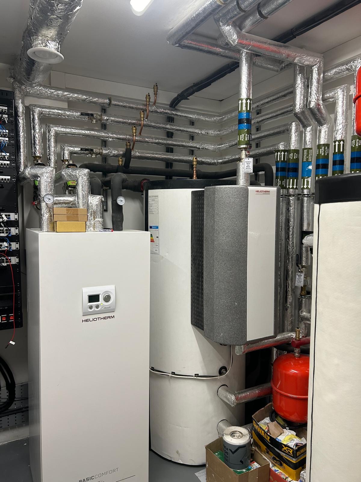Compact Heliotherm ground source heat pump plant with thermal storage and labelled distribution circuits.