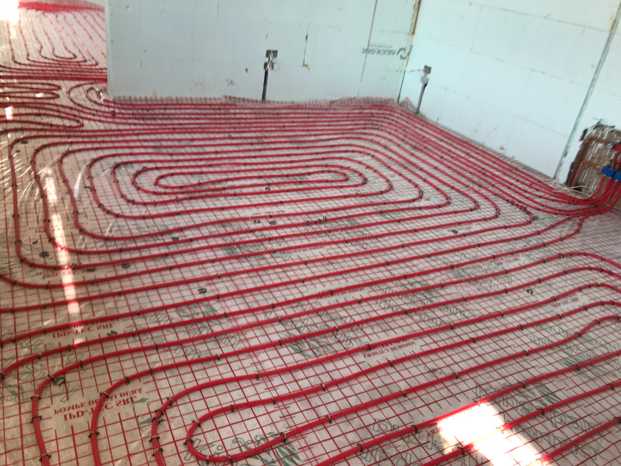 Dense red underfloor heating loops over insulation in a glazed room