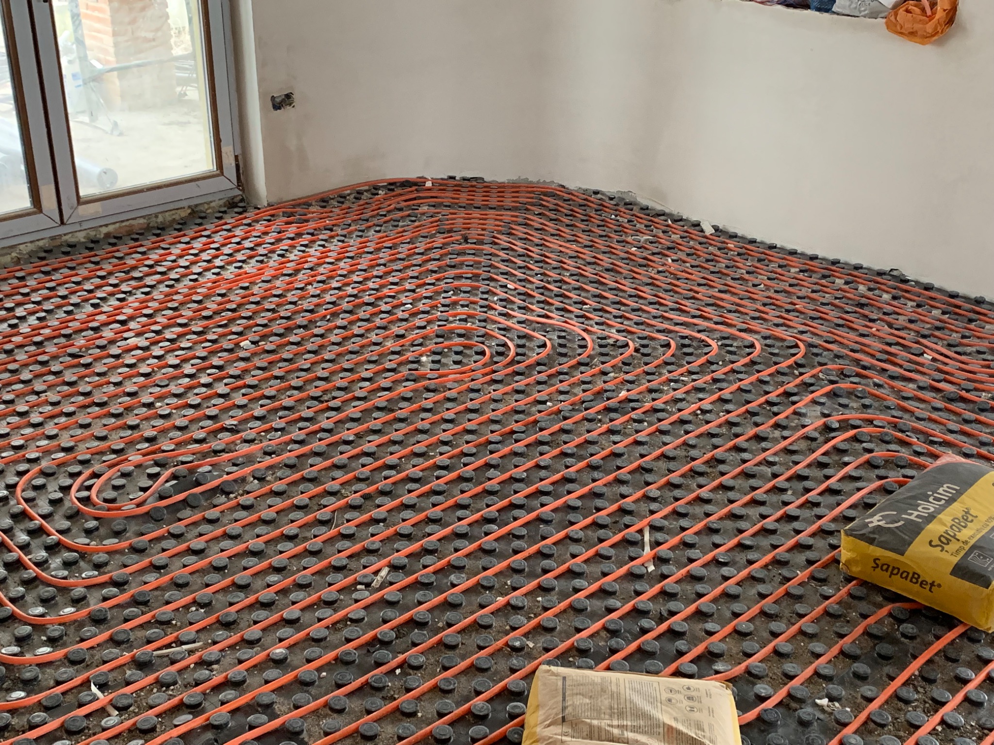 Castellated underfloor heating panels with orange pipe laid up to a window wall