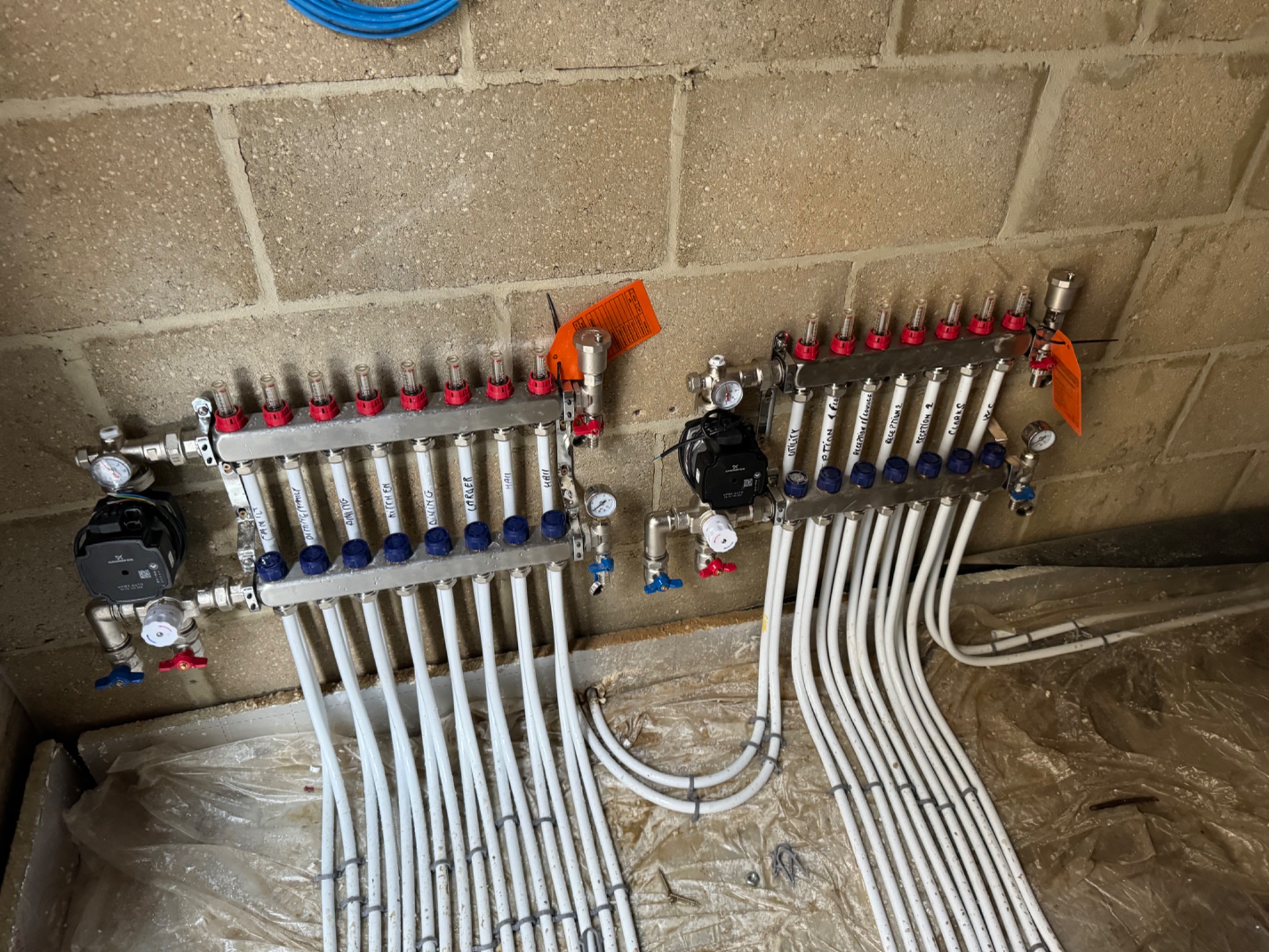 Two stainless steel underfloor heating manifolds with circulation pumps in a plant area