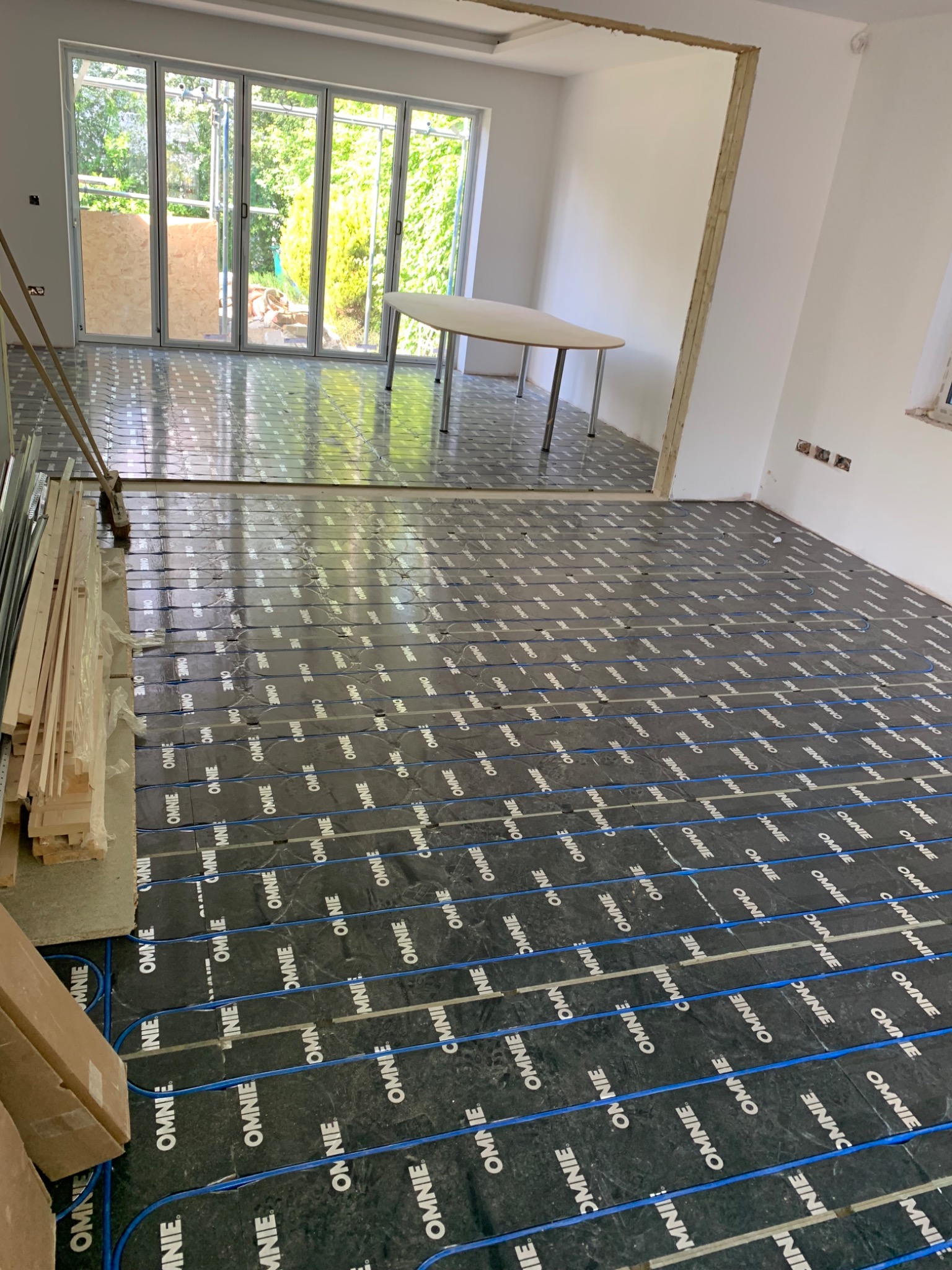 Foil-faced underfloor heating panels with blue pipe across an open-plan room