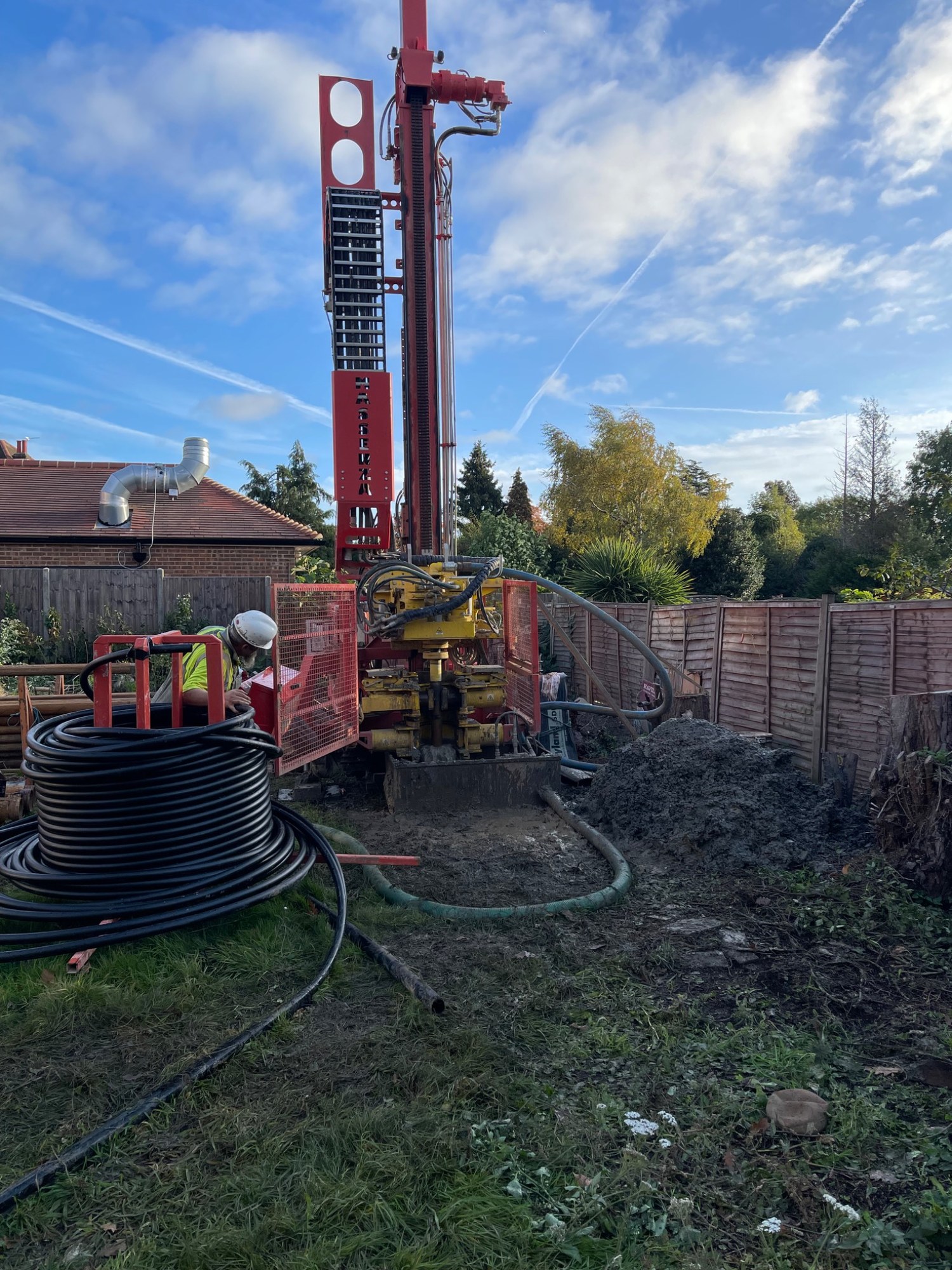 Vertical ground borehole drilling rig operating beside a residential property