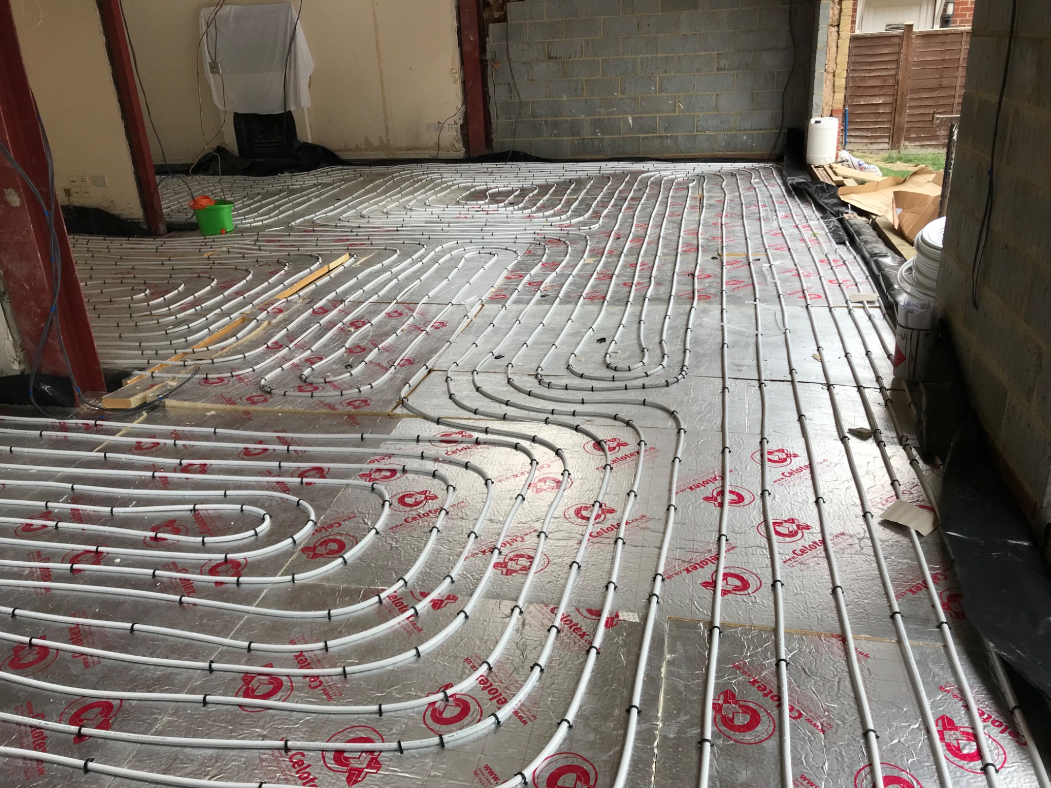 White underfloor heating pipes clipped over foil-faced insulation across a wide room