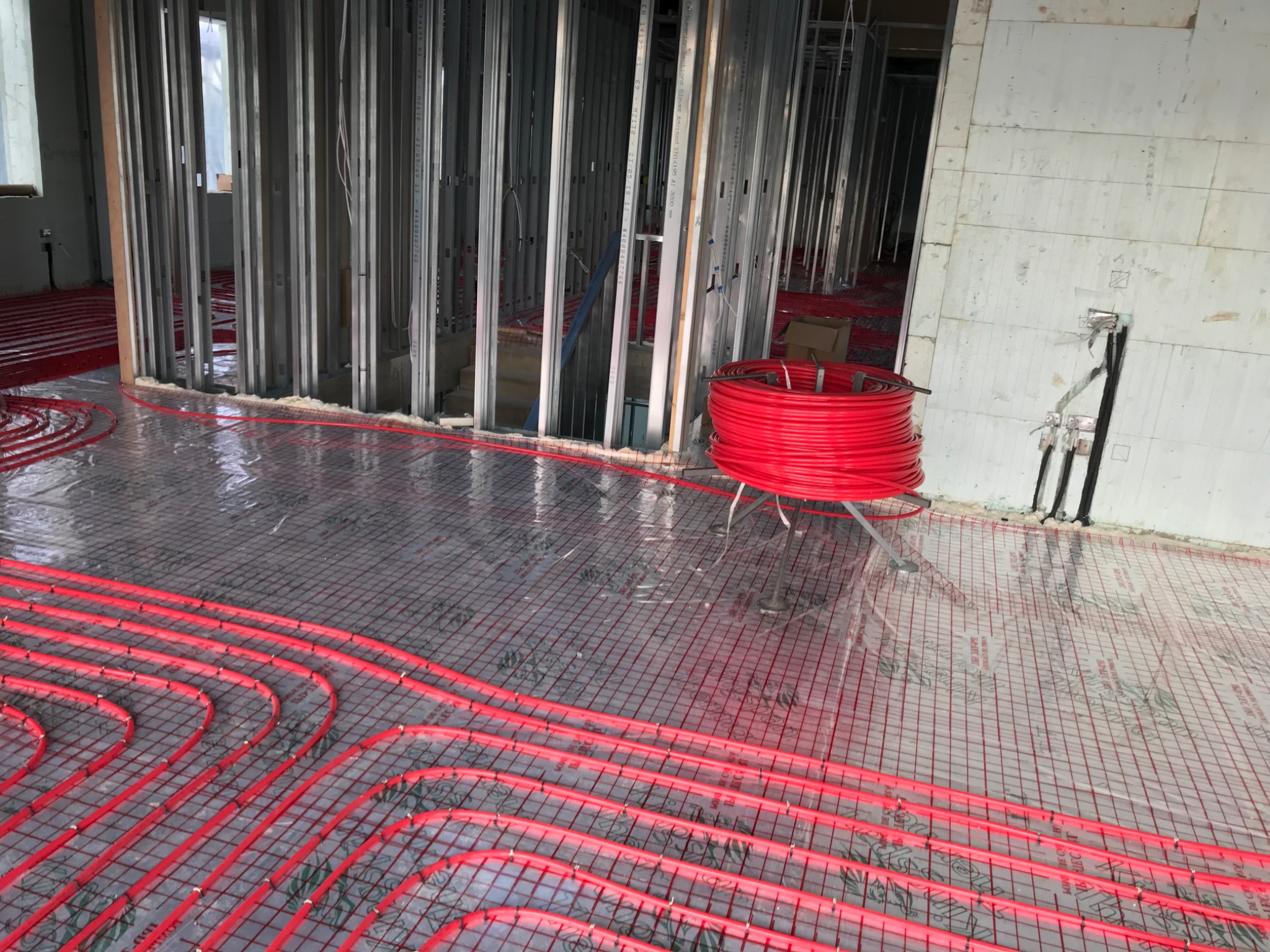 Red pipe coil on a decoiler beside installed underfloor heating loops