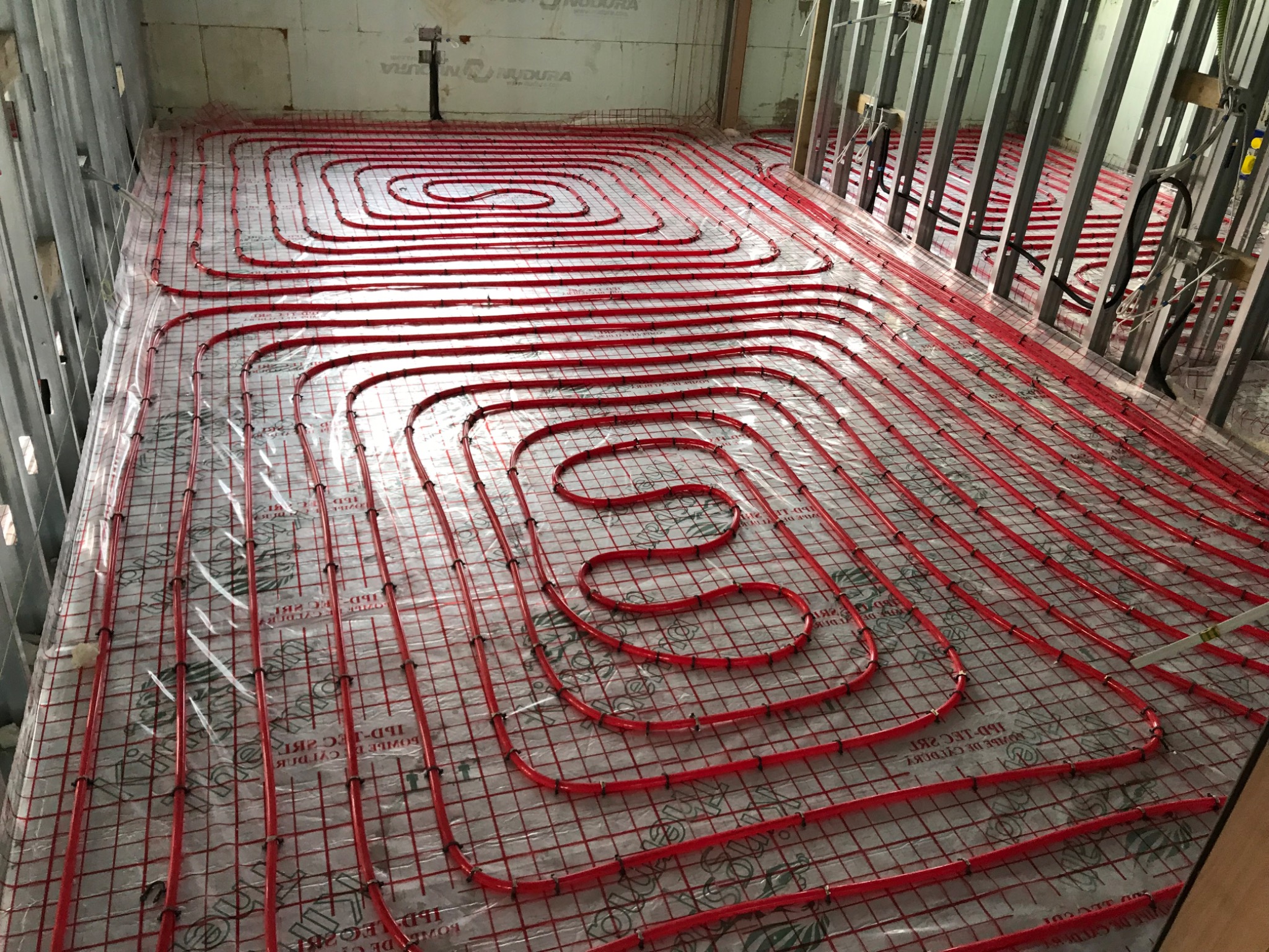 Red underfloor heating pipes tied to reinforcement mesh over a membrane