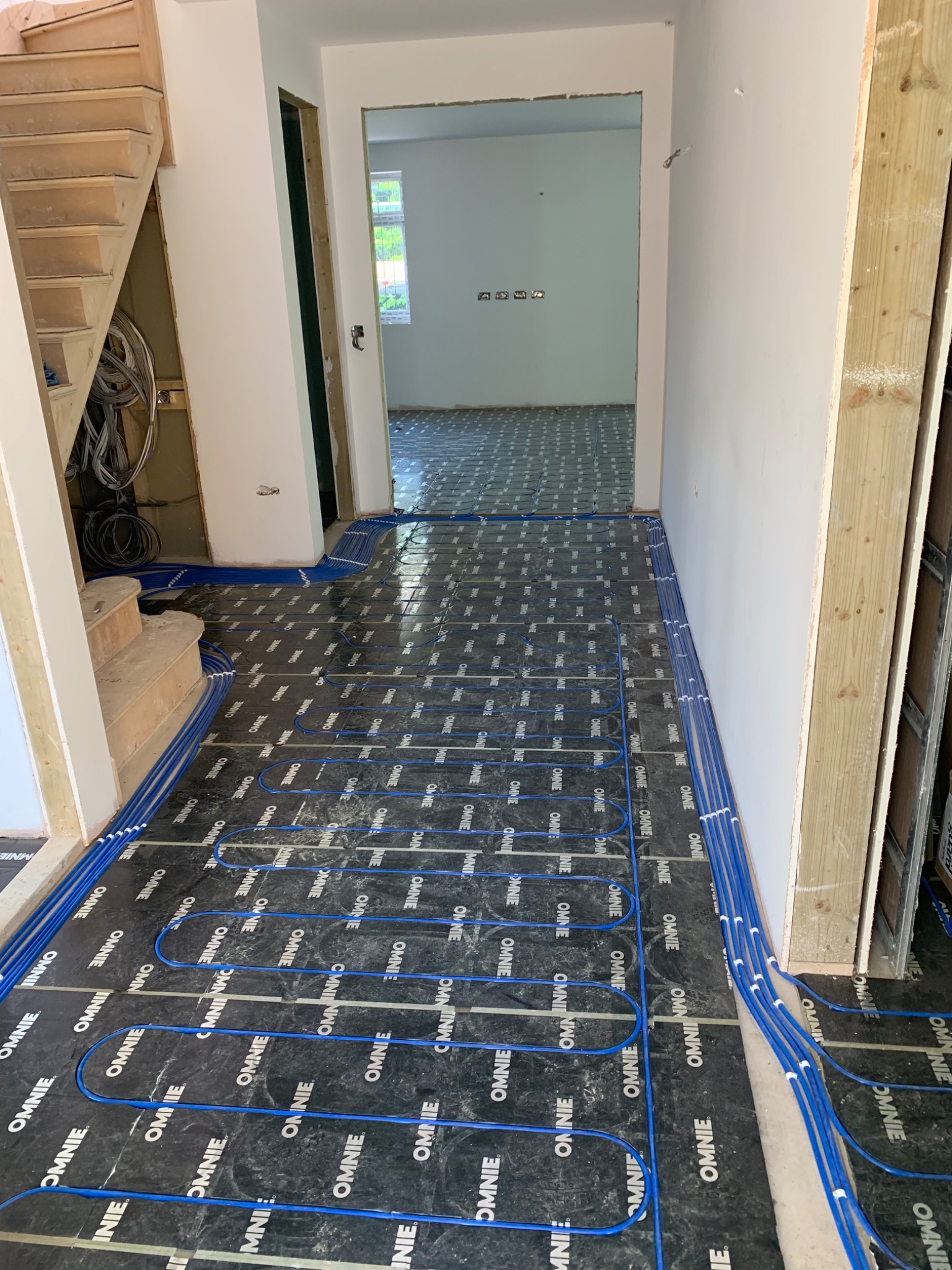 Blue underfloor heating pipe loops in a hallway routed around a staircase