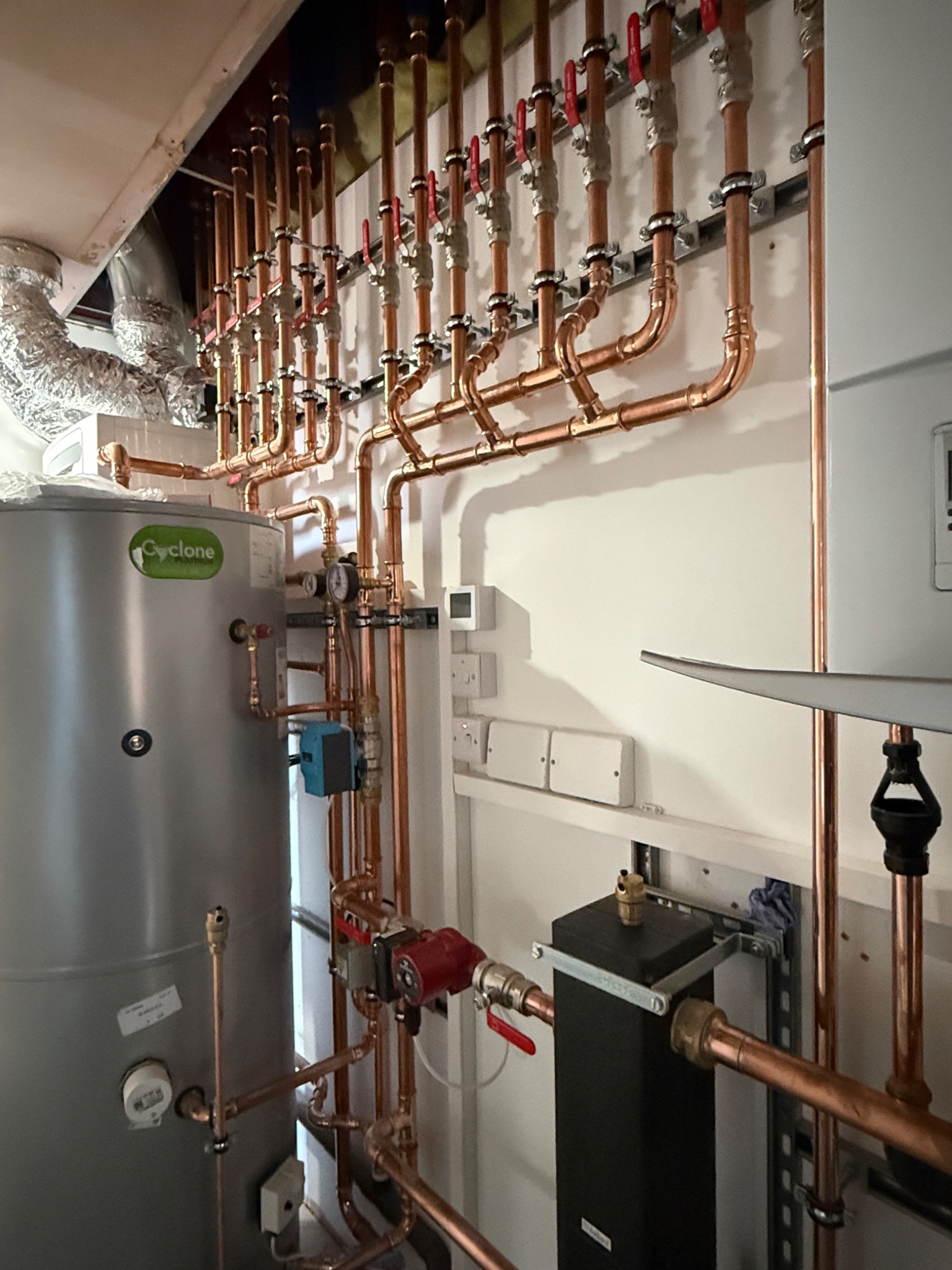 Copper pipework manifold with red-handled valves above a hot water cylinder