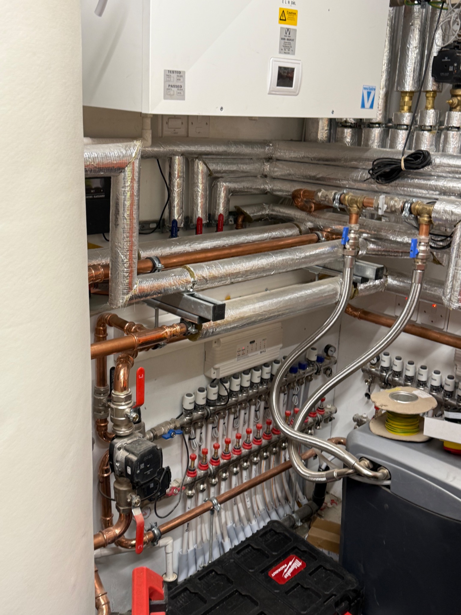 Plant room with insulated copper pipework, MVHR unit and underfloor heating manifolds