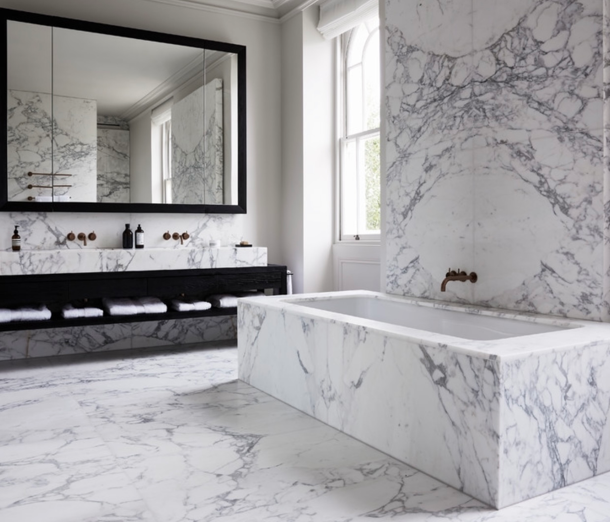 Marble bathroom with framed mirror, stone-clad bath and wall-mounted taps