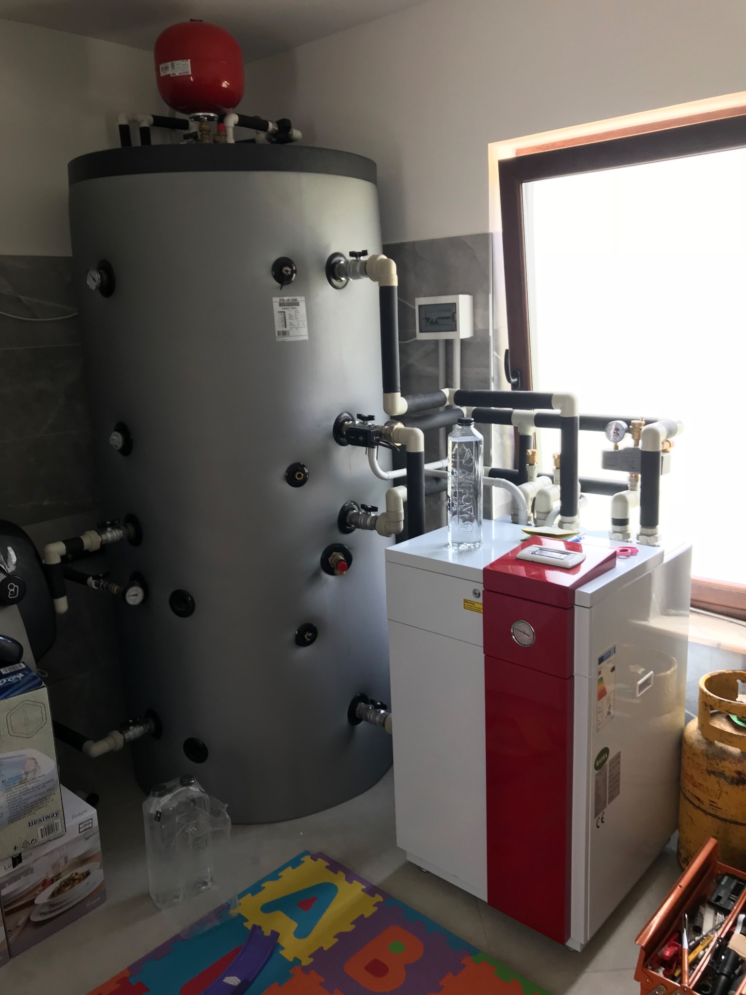 Grey buffer vessel with red expansion vessel beside a floor-standing heat pump