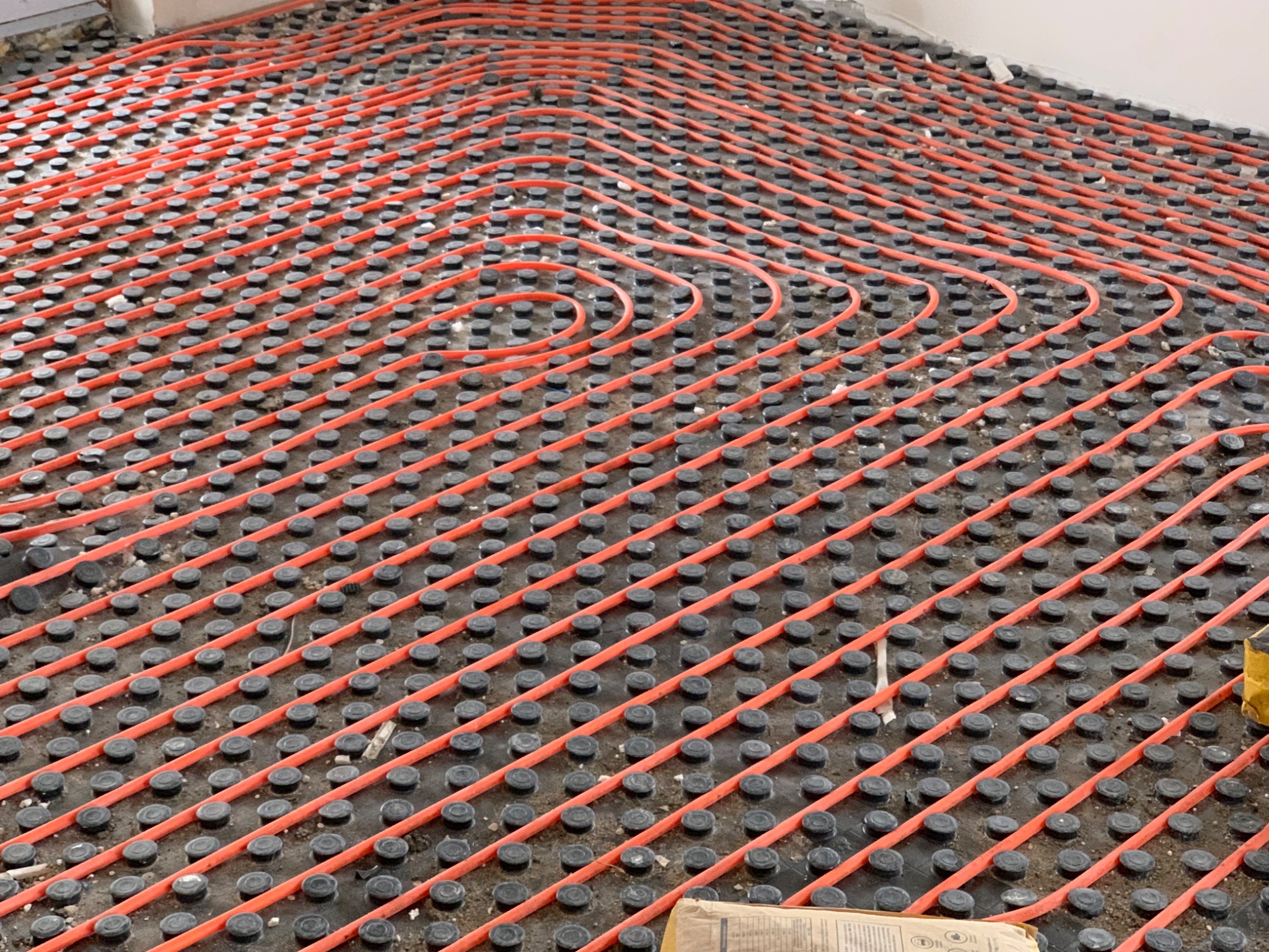 Orange underfloor heating pipe held in a black castellated floor panel